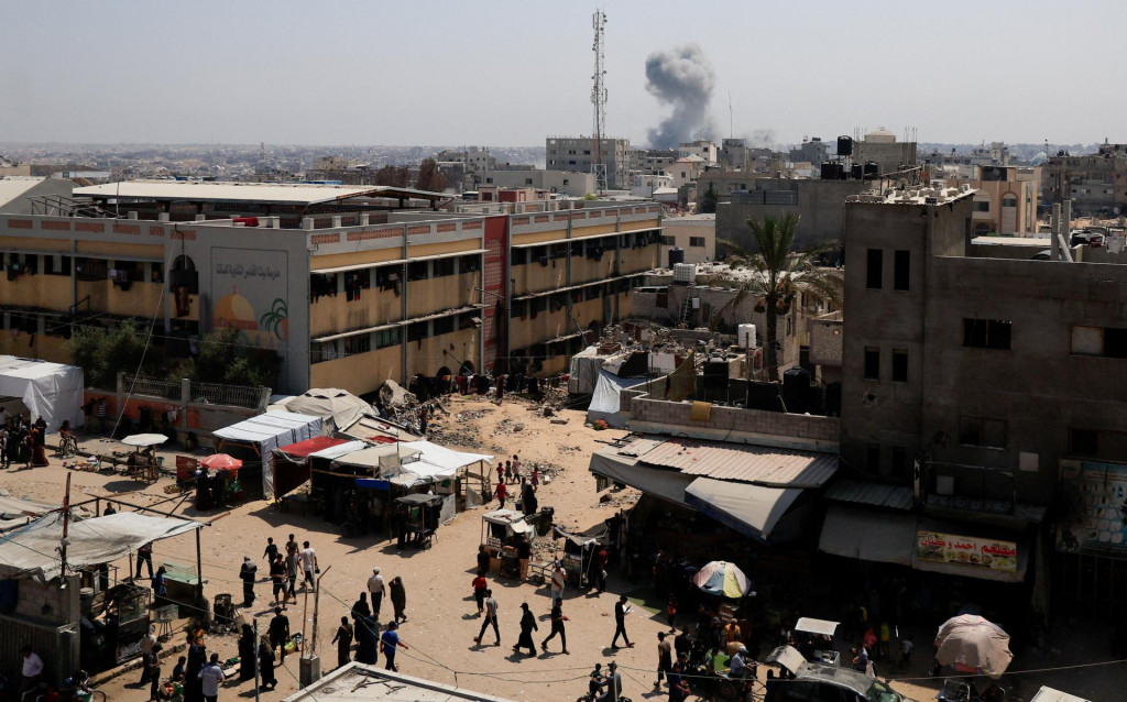 Palest&iacute;nčania kr&aacute;čaj&uacute;, zatiaľ čo v diaľke st&uacute;pa dym po izraelskom &uacute;toku v Ch&aacute;n J&uacute;nis v južnom P&aacute;sme Gazy. FOTO: Reuters