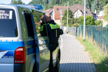 Policajt stojí pri policajnom vozidle počas razie v nemeckom Schleusingene. FOTO: TASR/DPA
