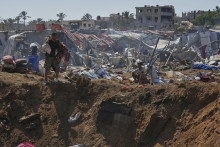 Palestínčania kráčajú pri okraji krátera po izraelských leteckých útokoch v utečeneckom tábore pre vysídlencov neďaleko nemocnice Al-Aksá v meste Dajr al-Balah, v centrálnom Pásme Gazy. FOTO: TASR/AP