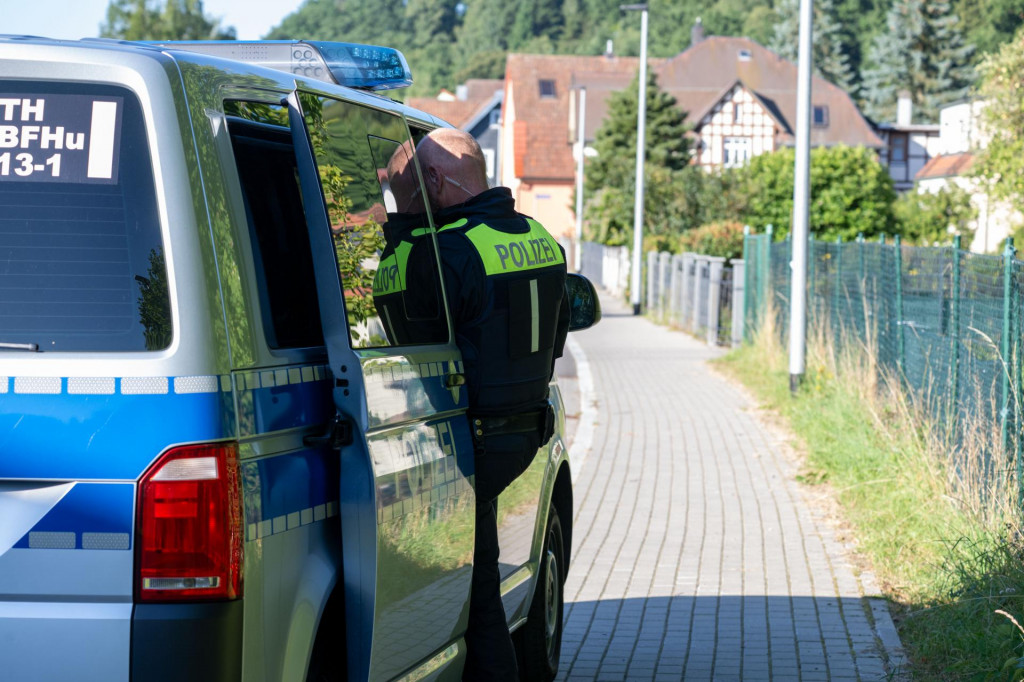 Policajt stojí pri policajnom vozidle počas razie v nemeckom Schleusingene. FOTO: TASR/DPA
