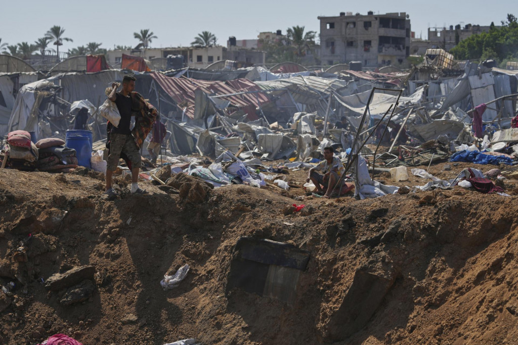 Palestínčania kráčajú pri okraji krátera po izraelských leteckých útokoch v utečeneckom tábore pre vysídlencov neďaleko nemocnice Al-Aksá v meste Dajr al-Balah, v centrálnom Pásme Gazy. FOTO: TASR/AP