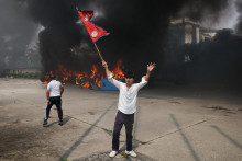 Demonštrant drží nepálsku vlajku, zatiaľ čo z parlamentného komplexu stúpa dym. FOTO: Reuters