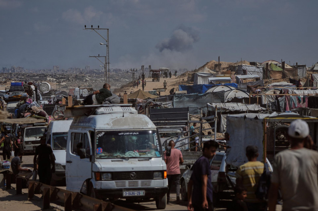 Dym stúpa nad mestom Gaza po izraelskom leteckom útoku, zatiaľčo vysídlení Palestínčania utekajú zo severného Pásma Gazy so svojimi vecami na ceste na juh cez Wadi Gazu 24. septembra 2025 po tom, ako izraelská armáda nariadila okamžitú evakuáciu celého mesta Gaza. FOTO: TASR/AP
