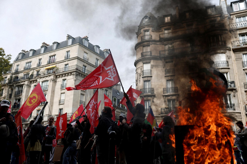 Protestujúci s vlajkami prechádzajú okolo horiaceho odpadkového koša počas demonštrácie v Paríži v rámci celoštátnych štrajkov a protestov proti vláde a možným úsporným opatreniam vo Francúzsku. FOTO: Reuters