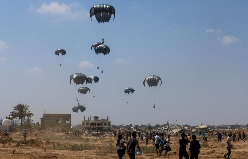 Palestínčania bežia k padákom s balíčkami pomoci v Deir Al-Balah v centrálnom pásme Gazy. FOTO: Reuters