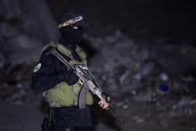 Militant Hamasu stojí na stráži, zatiaľ čo vozidlá Červeného kríža prevážajú telá rukojemníkov zadržiavaných v Gaze. FOTO: Reuters