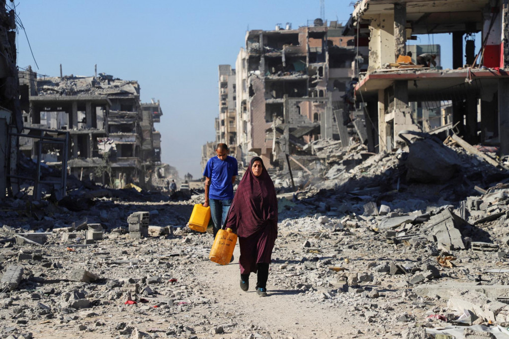Palestínčania prechádzajú okolo trosiek zničených budov v meste Gaza. FOTO: Reuters