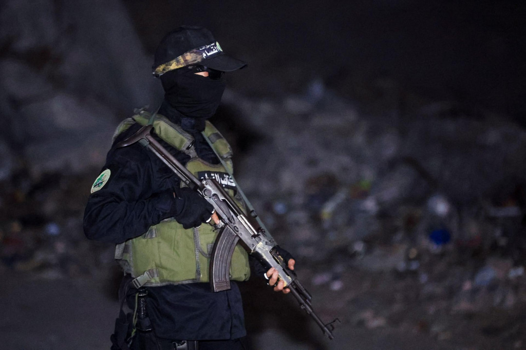 Militant Hamasu stojí na stráži, zatiaľ čo vozidlá Červeného kríža prevážajú telá rukojemníkov zadržiavaných v Gaze. FOTO: Reuters