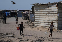 Palestínčania nesú bandasky a plastové fľaše na vodu v tábore pre vysídlencov v meste Gaza City. FOTO: TASR/AP