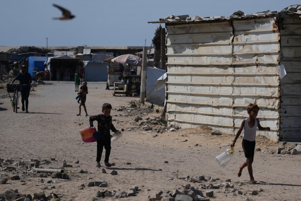 Palestínčania nesú bandasky a plastové fľaše na vodu v tábore pre vysídlencov v meste Gaza City. FOTO: TASR/AP