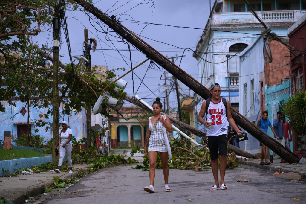 Ľudia kráčajú na ulici okolo spadnutých stĺpov elektrického vedenia po tom, ako túto oblasť zasiahol hurikán Melissa v Santiagu de Cuba 29. októbra 2025. FOTO: TASR/AP