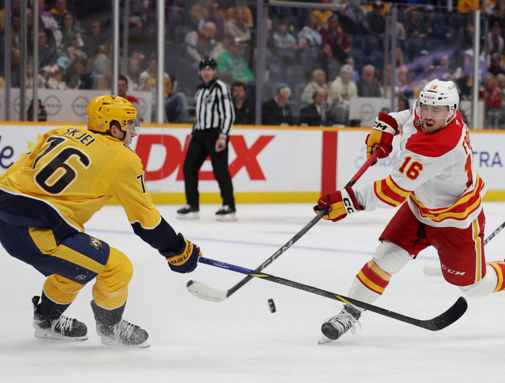 Center Calgary Flames Morgan Frost (16) strieľa, zatiaľ čo obranca Nashville Predators Brady Skjei (76) bráni počas druhej tretiny. FOTO: Alan Poizner/Imagn Images