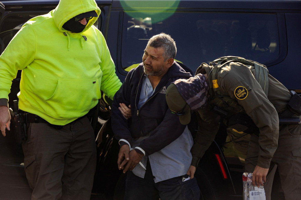 Americkí federálni agenti presúvajú zadržanú osobu z vozidla na mieste prepravy zadržaných počas imigračnej razie v Chicagu. FOTO: Reuters