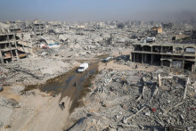 Palestínčania prechádzajú okolo trosiek zničených budov v meste Gaza. FOTO: Reuters