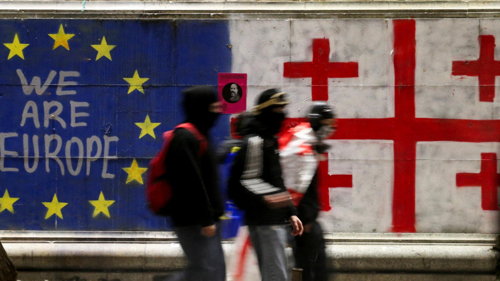Podporovatelia gruzínskych opozičných strán prechádzajú okolo múru namaľovaného vlajkou Európskej únie a gruzínskou vlajkou počas protestu proti rozhodnutiu vlády pozastaviť rokovania o vstupe do Európskej únie (8. decembra). FOTO: Reuters