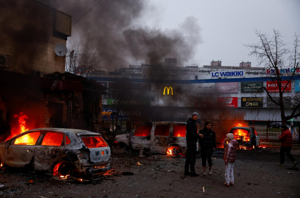 Ľudia sa zhromažďujú pri horiacich vozidlách poškodených počas ruského útoku na Kyjev. FOTO: Reuters
