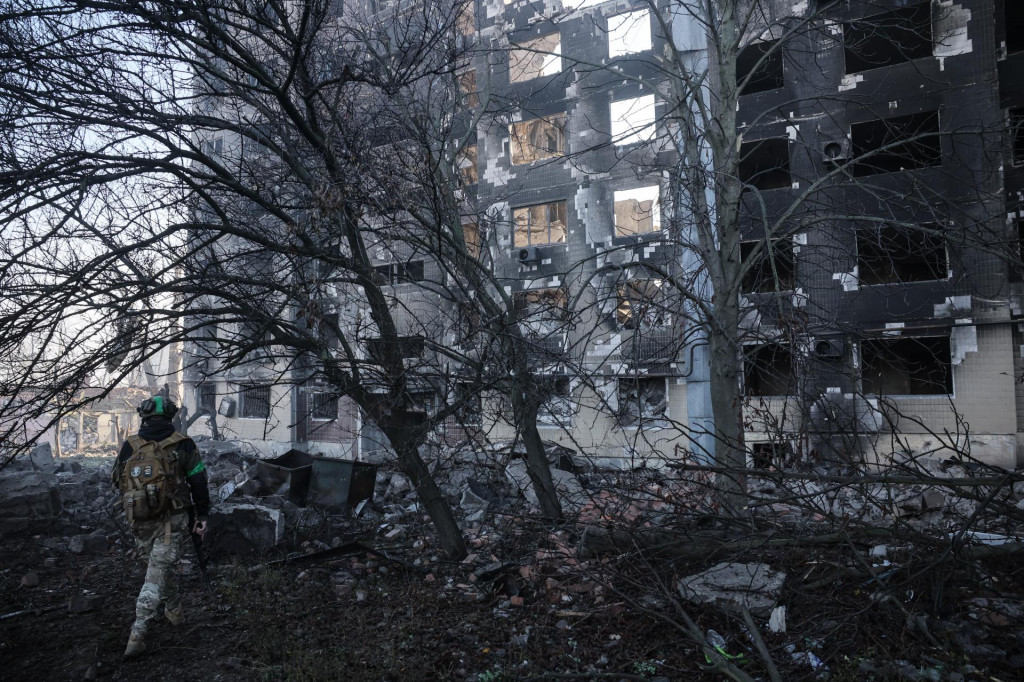 Ukrajinský vojak kráča na ulici pred zničenou obytnou budovou. FOTO: TASR/AP
