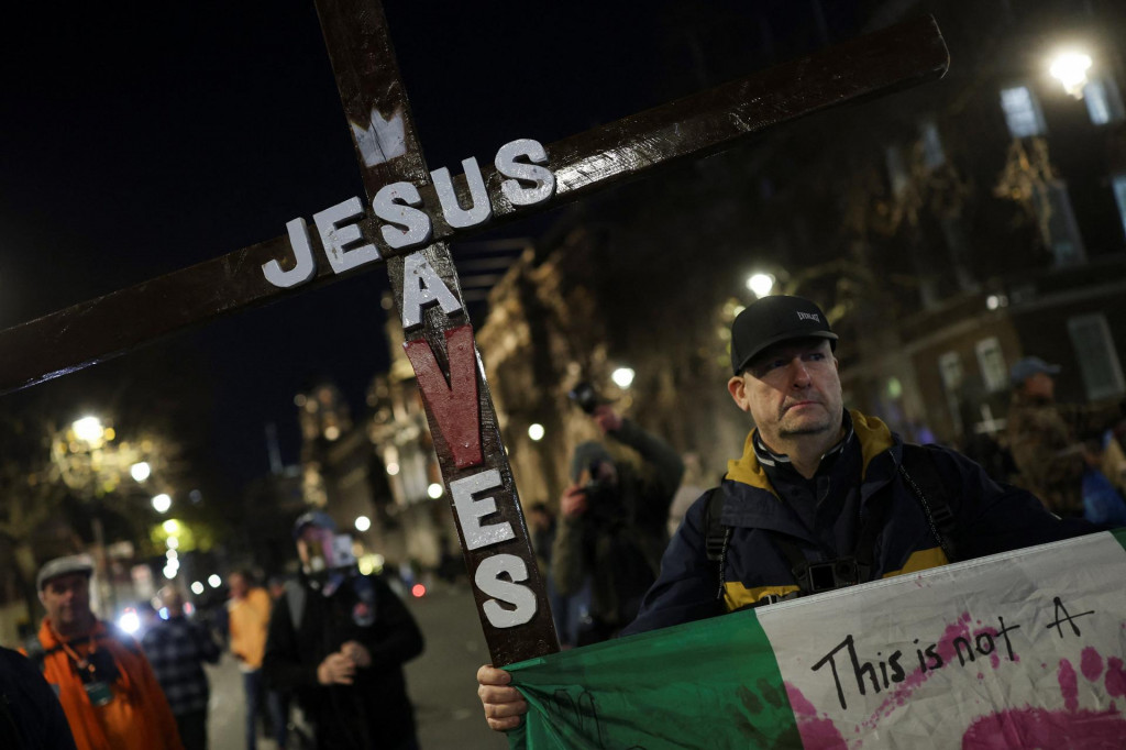 Muž drží drevený kríž s nápisom „Ježiš zachraňuje“ počas zhromaždenia „Vrátenie Krista späť do Vianoc“, ktoré zorganizoval protiimigračný aktivista Stephen Yaxley-Lennon, známy ako „Tommy Robinson“, a jeho hnutie Zjednoťte kráľovstvo neďaleko Downing Street v Londýne. FOTO: Reuters