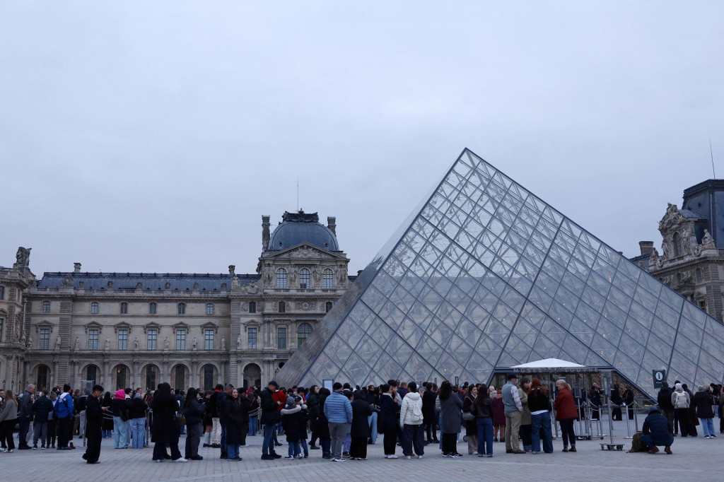Ľudia stoja pri sklenenej pyram&iacute;de m&uacute;zea Louvre, ktor&eacute; zost&aacute;va zatvoren&eacute;. FOTO: Reuters