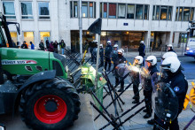 Policajti stoja pred traktormi eur&oacute;pskych farm&aacute;rov, ktor&yacute;mi blokuj&uacute; hlavn&uacute; ulicu počas demon&scaron;tr&aacute;cie proti rev&iacute;zii dot&aacute;ci&iacute;. FOTO: TASR/AP

