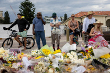 Ľudia sm&uacute;tia pri kvetinov&yacute;ch poct&aacute;ch za obete a pozostal&yacute;ch po masovej streľbe počas židovskej oslavy Chanuky na pl&aacute;ži Bondi Beach v Sydney. FOTO: Reuters