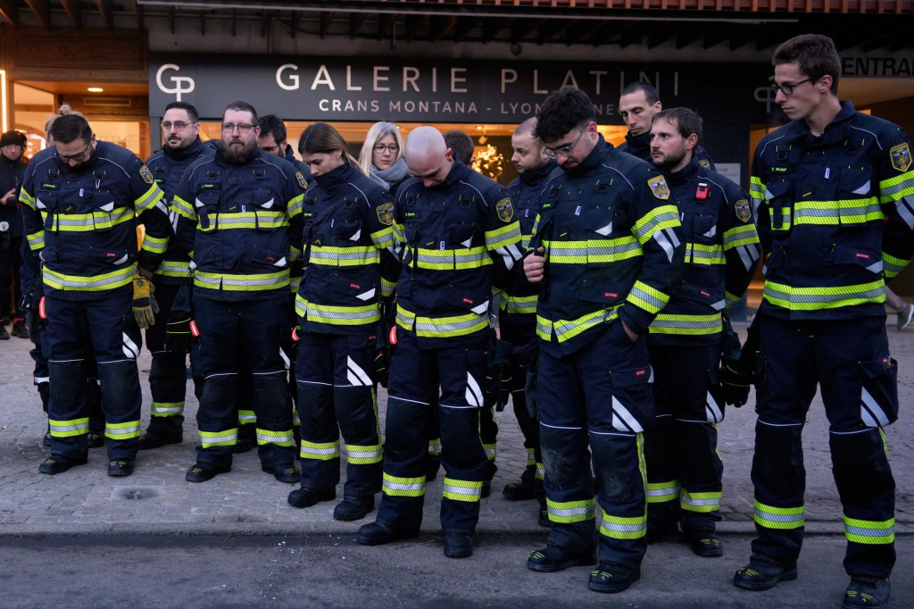 Hasiči, ktor&iacute; zasahovali pri požiari baru stoja v tichosti neďaleko vyhoren&eacute;ho baru Le Constellation v Crans-Montane vo &scaron;vajčiarskych Alp&aacute;ch 3. janu&aacute;ra 2026. FOTO: TASR/AP