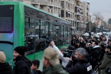 Ľudia sa zhromažďuj&uacute; pri autobuse, v ktorom sa vzdali pr&iacute;slu&scaron;n&iacute;ci S&yacute;rskych demokratick&yacute;ch s&iacute;l (SDF), v &scaron;tvrti &Scaron;ajch Maks&uacute;d po p&aacute;de dohody medzi s&yacute;rskou vl&aacute;dou a SDF. FOTO: Reuters