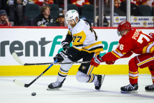 Obranca Pittsburgh Penguins Brett Kulak (77) drž&iacute; puk proti centru Calgary Flames Martinovi Posp&iacute;&scaron;ilovi (76) počas tretej tretiny. FOTO: Sergei Belski/Imagn Images