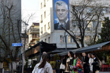 Ľudia kr&aacute;čaj&uacute; okolo transparentu s plag&aacute;tom b&yacute;val&eacute;ho kosovsk&eacute;ho prezidenta Hashima Thaciho v Pri&scaron;tine. FOTO: Reuters