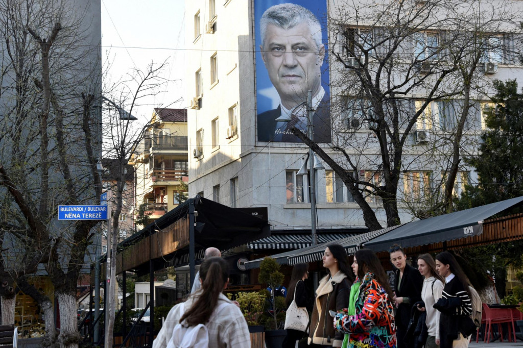 Ľudia kr&aacute;čaj&uacute; okolo transparentu s plag&aacute;tom b&yacute;val&eacute;ho kosovsk&eacute;ho prezidenta Hashima Thaciho v Pri&scaron;tine. FOTO: Reuters