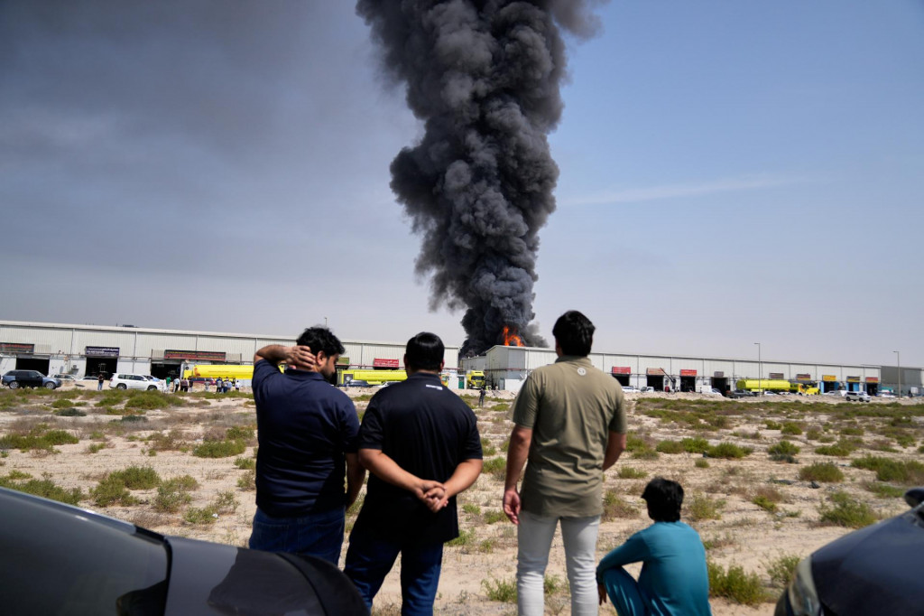 Ľudia sleduj&uacute; ako plamene a čierny dym st&uacute;paj&uacute; zo skladu v priemyselnej z&oacute;ne &Scaron;arjah City počas odvetn&eacute;ho &uacute;toku Ir&aacute;nu v Dubaji. FOTO: TASR/AP