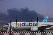 Lietadlo spoločnosti FlyDubai 16. marca parkuje na medzin&aacute;rodnom letisku v Dubaji, zatiaľ čo v pozad&iacute; st&uacute;pa dym po dronovom &uacute;toku na palivov&uacute; n&aacute;drž letiska. FOTO: TASR/AP