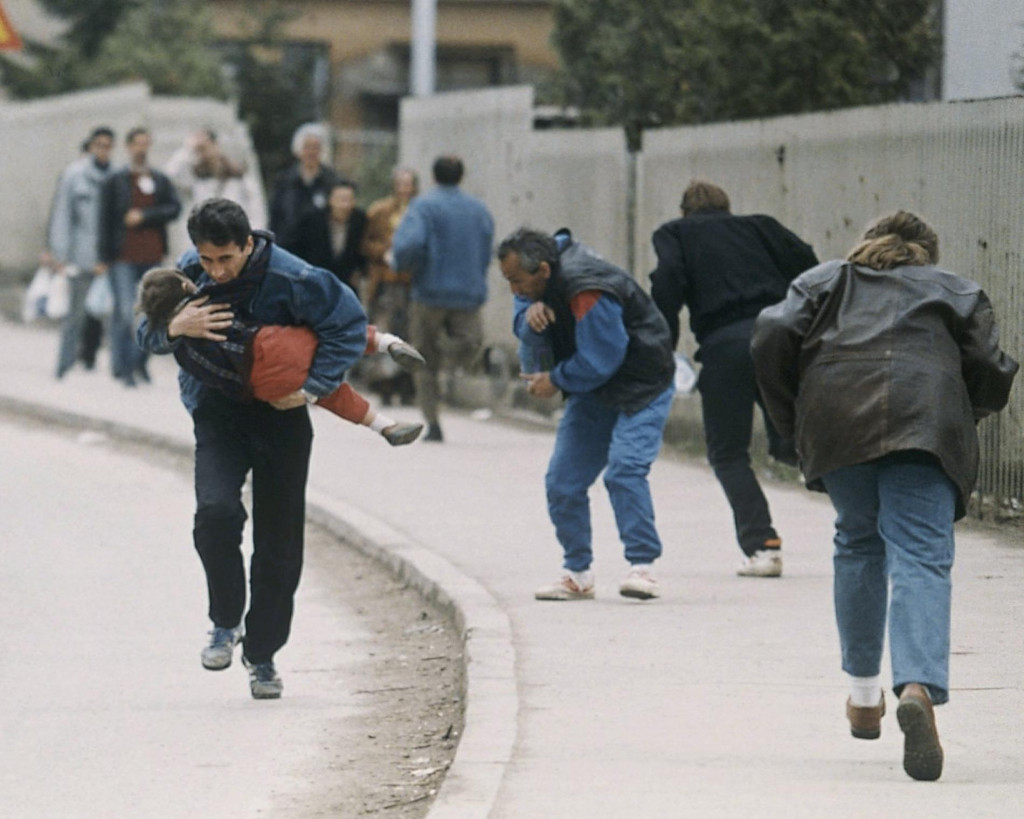 Muž drž&iacute; svoje dieťa, zatiaľ čo spolu s ostatn&yacute;mi bežia okolo jedn&eacute;ho z miest v Sarajeve, kde p&ocirc;sobili ostreľovači. FOTO: TASR/AP