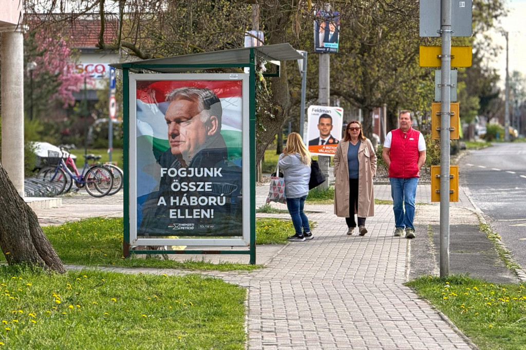Ľudia kr&aacute;čaj&uacute; okolo predvolebn&eacute;ho plag&aacute;tu maďarskej vl&aacute;dnej strany Fidesz s portr&eacute;tom premi&eacute;ra a predsedu Fideszu Viktora Orb&aacute;na s n&aacute;pisom &rdquo;Zomknime sa proti vojne!&rdquo;. FOTO: TASR/AP