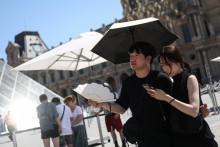 Dvaja ľudia sa ukr&yacute;vaj&uacute; pod d&aacute;ždnikom a použ&iacute;vaj&uacute; ventil&aacute;tor pred Louvrom uprostred silnej vlny hor&uacute;čav v Par&iacute;ži vo Franc&uacute;zsku. FOTO: Reuters