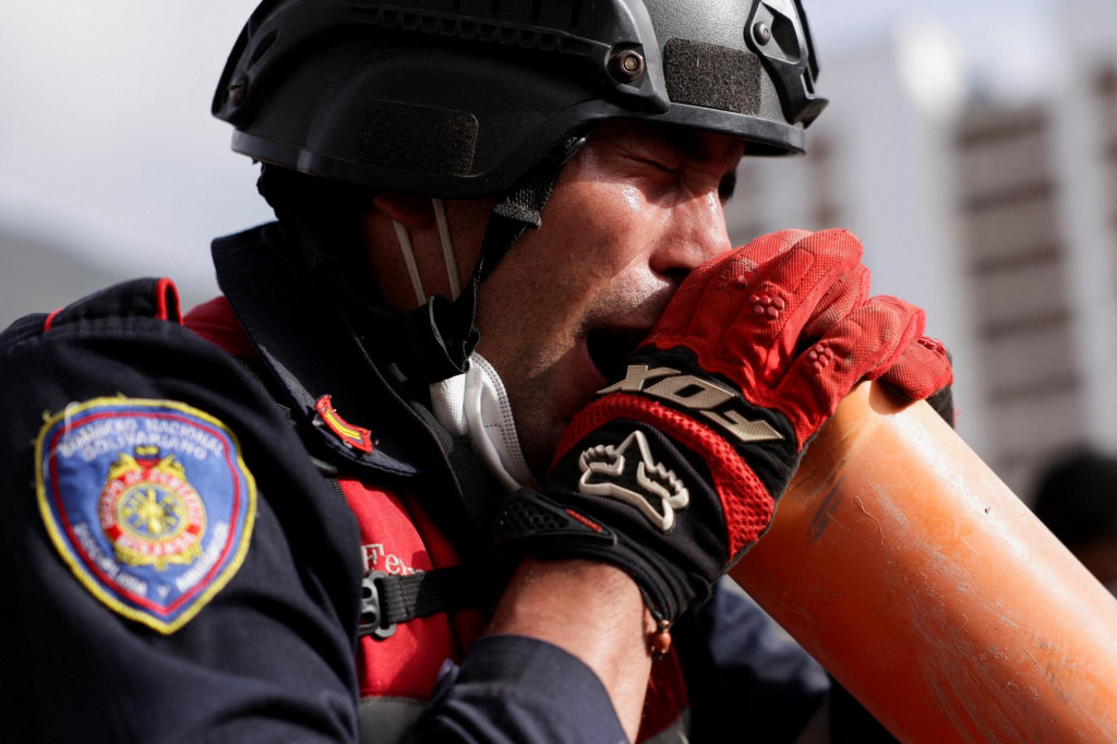 Hasič krič&iacute; cez hasičsk&uacute; r&uacute;ru na ľud&iacute; pod troskami zr&uacute;tenej budovy po zemetraseniach, ktor&eacute; zasiahli Venezuelu. FOTO: Reuters