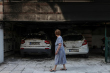 Žena prech&aacute;dza okolo po&scaron;koden&yacute;ch &aacute;ut a budovy po tom, čo &uacute;točn&iacute;ci v severogr&eacute;ckom meste Sol&uacute;n zap&aacute;lili tri obytn&eacute; budovy spojen&eacute; s vl&aacute;dnucou stranou. FOTO: Reuters