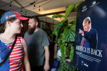 Ľudia s&uacute; v&iacute;tan&iacute; plag&aacute;tom americk&eacute;ho prezidenta Donalda Trumpa na v&yacute;stave Ministerstva poľnohospod&aacute;rstva USA na Veľkom americkom &scaron;t&aacute;tnom veľtrhu pri pr&iacute;ležitosti 250. v&yacute;ročia nez&aacute;vislosti USA vo Washingtone. FOTO: Reuters