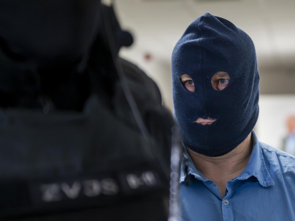 Kľ&uacute;čov&yacute; svedok Zolt&aacute;n Andrusk&oacute; v kukle prich&aacute;dza v sprievode pr&iacute;slu&scaron;n&iacute;kov Zboru v&auml;zenskej a justičnej str&aacute;že na s&uacute;dne pojedn&aacute;vanie v kauze objedn&aacute;vky vraždy novin&aacute;ra J&aacute;na Kuciaka. FOTO: TASR/Martin Baumann