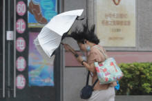Žena sa snaž&iacute; udržať d&aacute;ždnik počas tajf&uacute;nu Bavi v Tchaj-čungu na severe Taiwanu. FOTO: TASR/AP