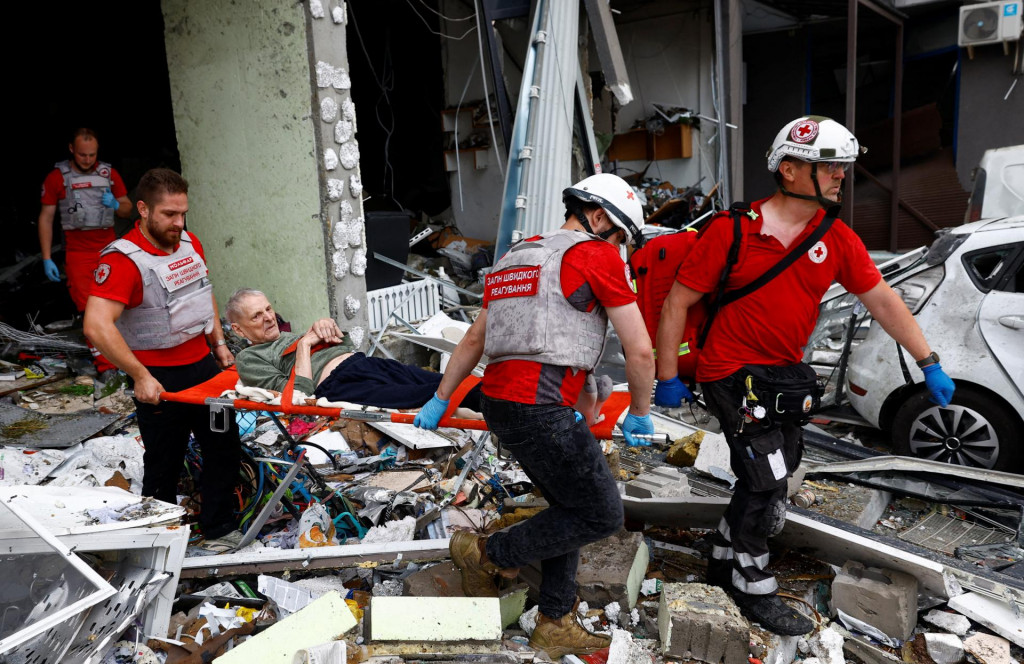 Dobrovoľn&iacute;ci Červen&eacute;ho kr&iacute;ža vyn&aacute;&scaron;aj&uacute; osobu z bytov&eacute;ho domu, ktor&yacute; bol ťažko po&scaron;koden&yacute; počas rusk&yacute;ch &uacute;tokov v Kyjeve. FOTO: Reuters