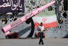 Muž kr&aacute;ča vedľa symbolickej makety ir&aacute;nskej rakety a ir&aacute;nskej vlajky v Teher&aacute;ne. FOTO: Reuters/WANA