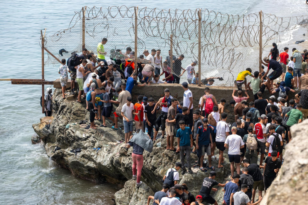 Migranti prech&aacute;dzaj&uacute; cez ostnat&yacute; dr&ocirc;t pri pokuse prekročiť hranicu z Maroka do &scaron;panielskej enkl&aacute;vy Ceuta. FOTO: TASR/AP