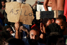 Migranti držia n&aacute;pisy &bdquo;azyl&ldquo; v &scaron;panielčine, zatiaľ čo čakaj&uacute; v rade na jedlo a n&aacute;poje od Červen&eacute;ho kr&iacute;ža po hromadnom prekročen&iacute; hranice pe&scaron;o a po mori z Maroka na &scaron;panielske &uacute;zemie v Ceute. FOTO: Reuters