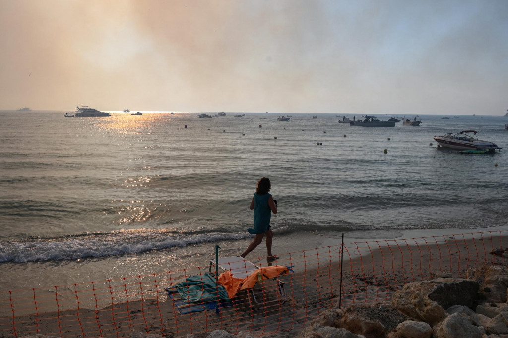 Žena bež&iacute; smerom k pr&iacute;stavu, aby bola evakuovan&aacute; z letoviska Siviri po lesnom požiari rozd&uacute;chanom siln&yacute;m vetrom na polostrove Chalkidiki v Gr&eacute;cku. FOTO: Reuters