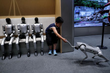 Dieťa sed&iacute; vedľa humanoidn&yacute;ch robotov G1 spoločnosti Unitree a interaguje s robotom GO2 tej istej firmy v predajni Unitree v Pekingu 1. augusta 2026. FOTO: Reuters