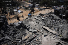 Palest&iacute;nčania kr&aacute;čaj&uacute; okolo zničen&eacute;ho skladu s potravinovou pomocou po izraelsk&yacute;ch leteck&yacute;ch &uacute;tokoch v meste Dajr al-Balah, v centr&aacute;lnom P&aacute;sme Gazy. FOTO: TASR/AP