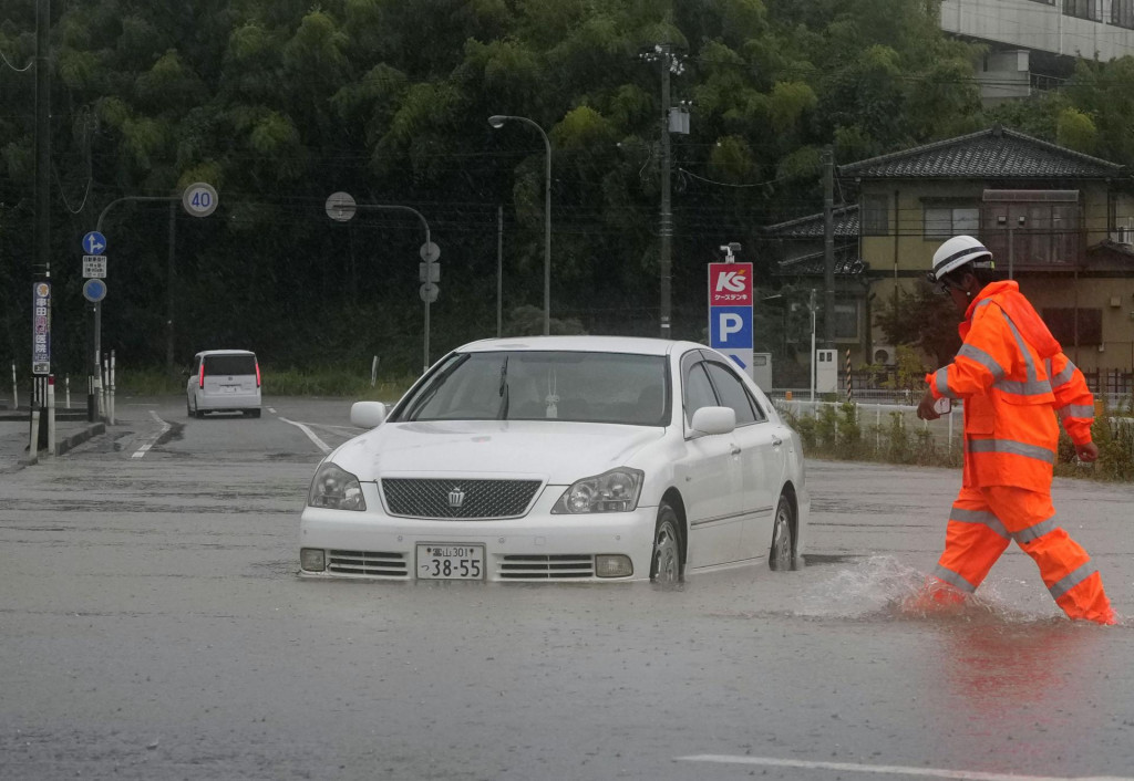 Auto jazd&iacute; po zaplavenej ulici po prudk&yacute;ch dažďoch v japonskom meste Himi. FOTO: TASR/AP