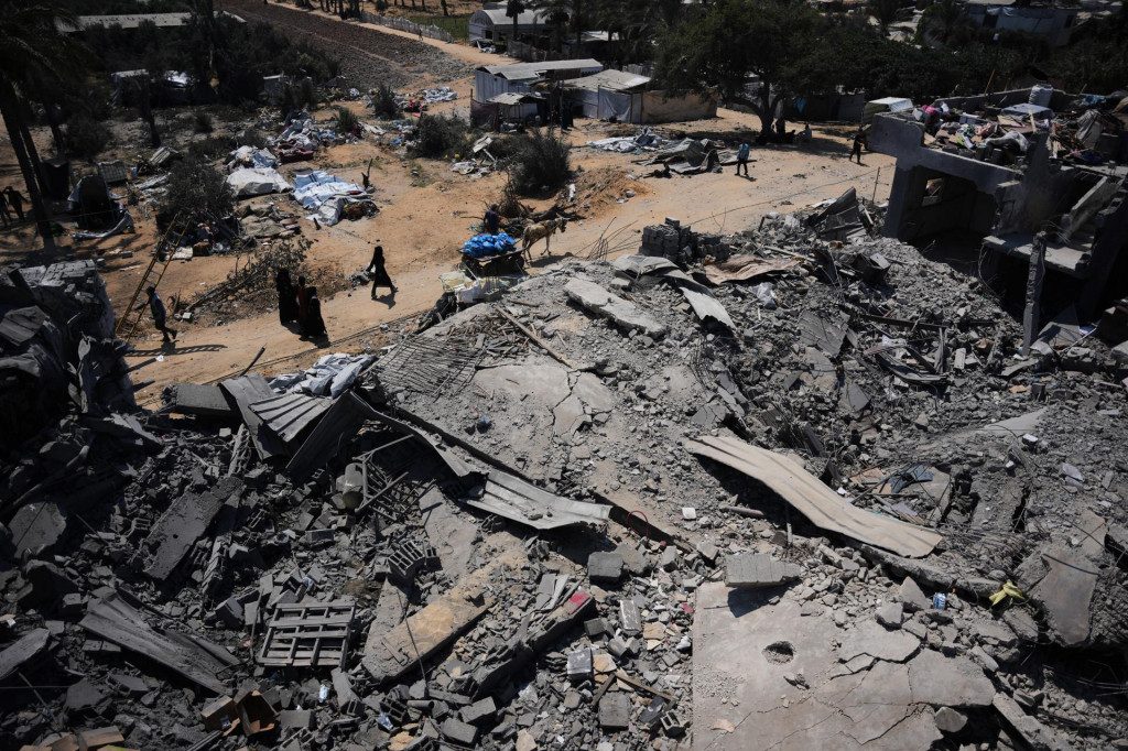 Palest&iacute;nčania kr&aacute;čaj&uacute; okolo zničen&eacute;ho skladu s potravinovou pomocou po izraelsk&yacute;ch leteck&yacute;ch &uacute;tokoch v meste Dajr al-Balah, v centr&aacute;lnom P&aacute;sme Gazy. FOTO: TASR/AP
