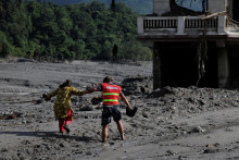 Z&aacute;chran&aacute;r pom&aacute;ha žene prejsť cez zablaten&uacute; cestu po bleskov&yacute;ch povodniach a zosuvoch p&ocirc;dy v Nep&aacute;le. FOTO: Reuters